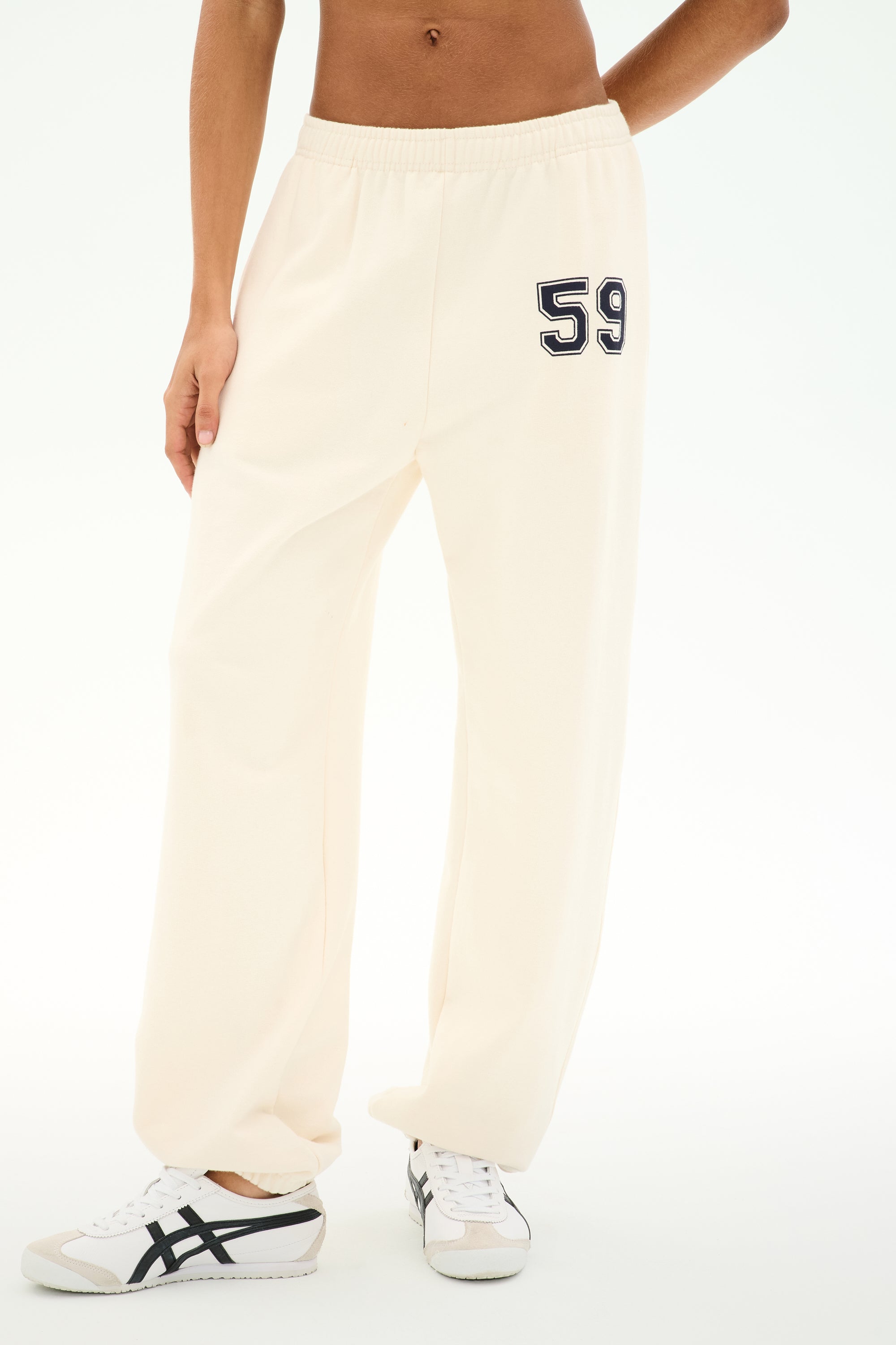 Dressed in the SPLITS59 Serena French Terry Oversized Sweatpant in creme, featuring soft cotton fabric and the number 59 printed on the left hip, paired with white sneakers.