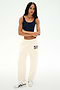 A person stands against a white background wearing a navy tank top, SPLITS59 Serena French Terry Oversized Sweatpant in Creme/59 made from soft cotton fabric, and white sneakers with a black design.