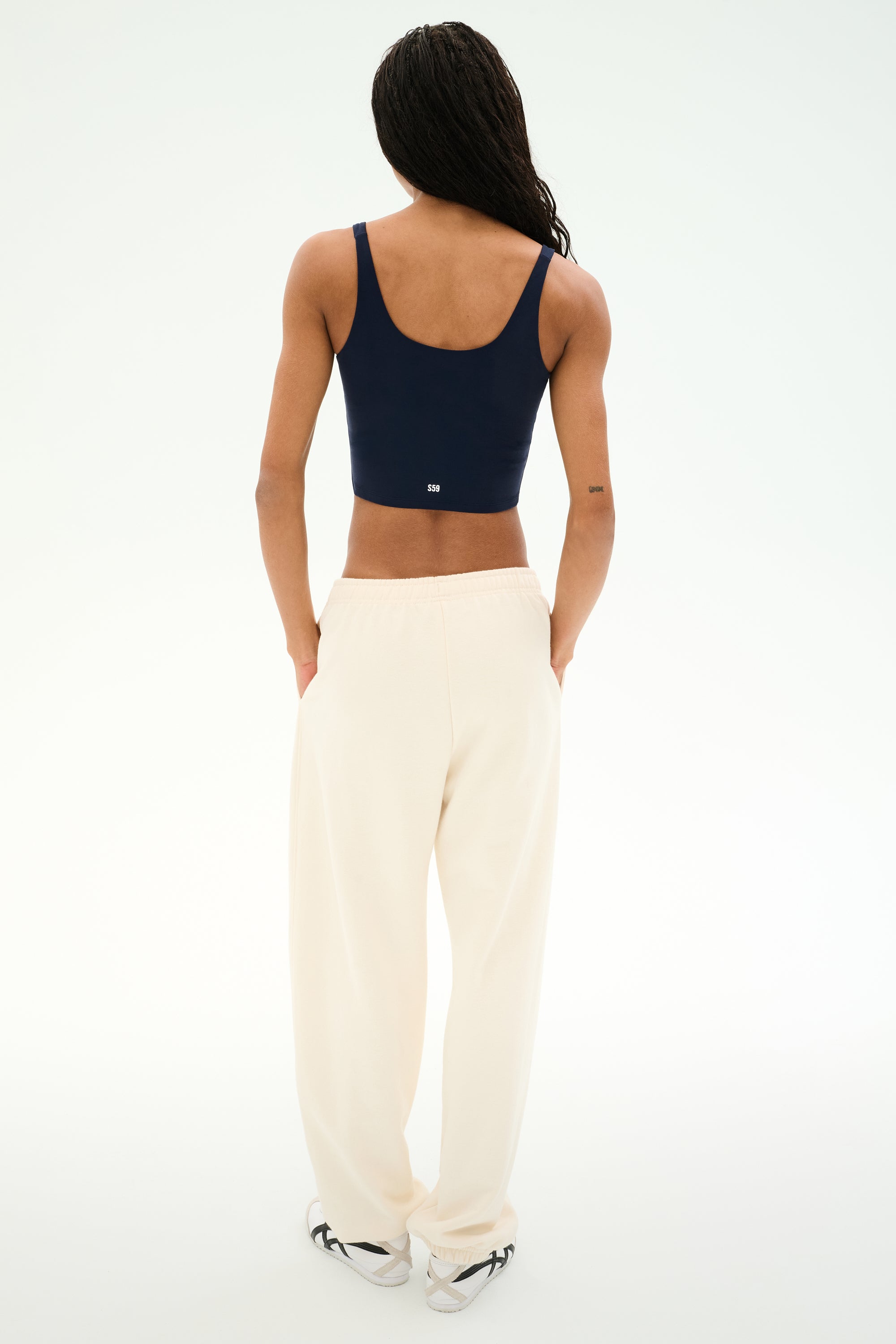 A person stands with their back to the camera against a plain white background, wearing a navy cotton tank top, white sneakers, and the SPLITS59 Serena French Terry Oversized Sweatpant in Creme/59.