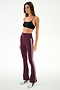 A woman stands against a plain background, wearing the SPLITS59 Raquel High Waist Supplex Flare leggings in Dark Cherry/Creme—a maroon, high-waisted flared design featuring white stripes and crafted from a comfortable nylon-spandex blend. She pairs them with a black sports bra and finishes the look with white sneakers accented by black details.