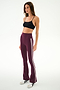 A woman stands against a plain background, wearing the SPLITS59 Raquel High Waist Supplex Flare leggings in Dark Cherry/Creme—a maroon, high-waisted flared design featuring white stripes and crafted from a comfortable nylon-spandex blend. She pairs them with a black sports bra and finishes the look with white sneakers accented by black details.