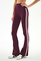 A person wearing the SPLITS59 Raquel High Waist Supplex Flare leggings in Dark Cherry/Creme—a comfortable nylon-spandex blend designed with two white side stripes—paired with white sneakers and standing against a plain background.