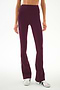 A person wears the SPLITS59 Raquel High Waist Supplex Flare leggings in Dark Cherry/Creme, featuring a high-waisted fit, soft spandex fabric, and white stripe detailing, paired with white sneakers and standing against a plain background.
