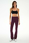 A woman wearing a black nylon-spandex crop top, SPLITS59 Raquel High Waist Supplex Flare pants in Dark Cherry/Creme, and white sneakers stands against a plain white background.