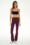 A woman wearing a black nylon-spandex crop top, SPLITS59 Raquel High Waist Supplex Flare pants in Dark Cherry/Creme, and white sneakers stands against a plain white background.