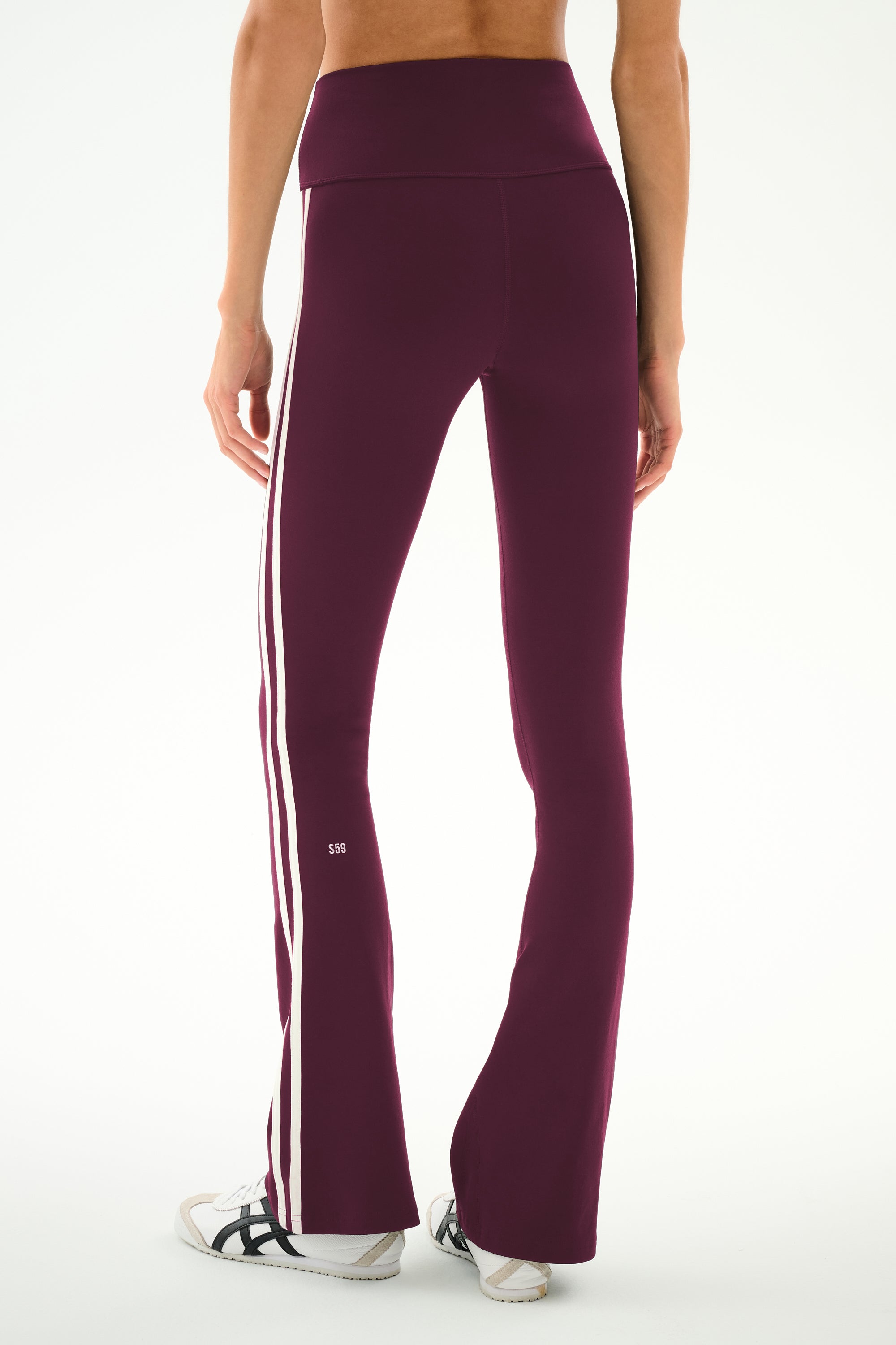 A person is shown from the back wearing the SPLITS59 Raquel High Waist Supplex Flare leggings in Dark Cherry/Crème, crafted from a comfortable spandex-nylon blend with two white side stripes. They are also wearing white sneakers with black stripes.