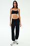 A woman stands against a plain background in SPLITS59’s Andie Oversized Fleece Varsity 59 Sweatpant in Black, paired with a black sports bra and white sneakers—perfect fleece joggers for cool weather workouts. Made in Los Angeles.