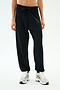 A person wears SPLITS59's Andie Oversized Fleece Varsity 59 Sweatpant in black, featuring a "59" on the left thigh, paired with white sneakers—ideal for cool weather workouts—standing against a plain white background.
