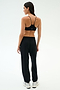 A woman stands with her back to the camera in SPLITS59’s Andie Oversized Fleece Varsity 59 Sweatpant - Black/59, paired with a black sports bra and white sneakers, ideal for cool weather workouts against a plain light background.