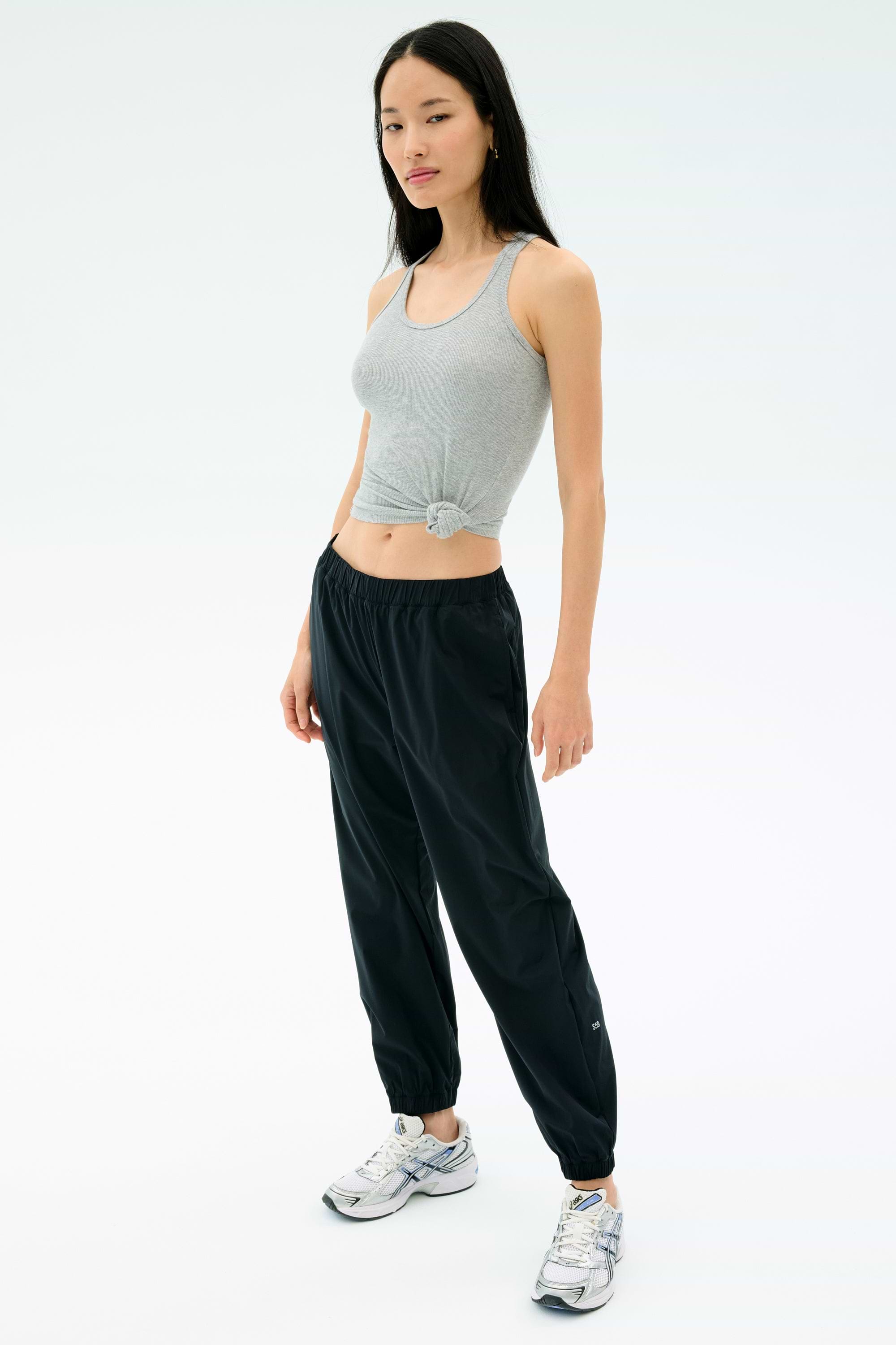 A woman faces forward, wearing the Splits59 Ashby Rib Tank in Lt. Heather Grey, paired with black jogger pants and white athletic sneakers, set against a plain white background.