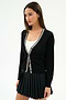 A woman in the SPLITS59 Bekah Knit Cardigan - Black/White over a white top and black pleated skirt stands against a plain white background.