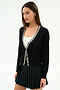 A woman in the SPLITS59 Bekah Knit Cardigan - Black/White over a white top and black pleated skirt stands against a plain white background.