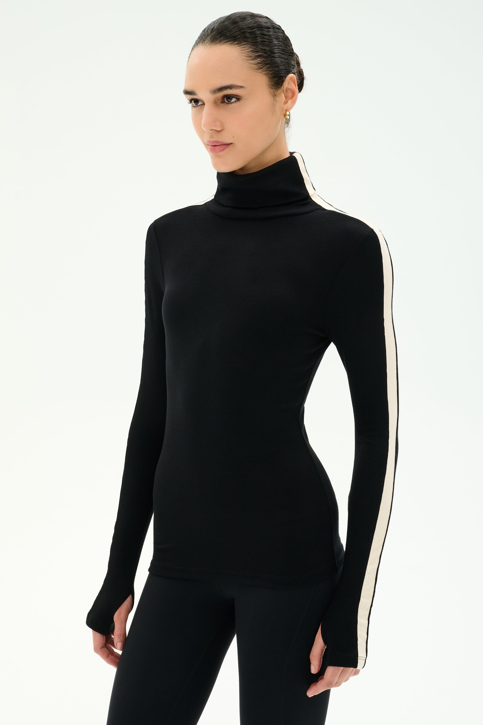 A woman wears the SPLITS59 Jackson Rib Full Length Turtleneck in Black/Creme, featuring a white stripe down the sleeve, as she stands against a plain light background.