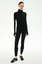 A woman stands against a plain white background wearing the SPLITS59 Jackson Rib Full Length Turtleneck in Black/Creme—a sleek black baby rib turtleneck with creme stripes on the sleeves—paired with black leggings and black sneakers featuring white stripes.