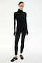 A woman stands against a plain white background wearing the SPLITS59 Jackson Rib Full Length Turtleneck in Black/Creme—a sleek black baby rib turtleneck with creme stripes on the sleeves—paired with black leggings and black sneakers featuring white stripes.