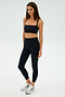 A person in a SPLITS59 Monah Rigor Bra - Black and black leggings stands against a plain background, with long hair and wearing white and gray sneakers, ready for gym workouts.
