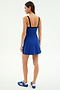 A woman stands with her back to the camera wearing the SPLITS59 Monah Rigor Dress in Cobalt/Black, featuring black straps, paired with blue athletic shoes, set against a plain white background.