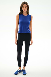 Woman standing against a white background, wearing the SPLITS59 Nikki Jersey Tank - Cobalt, black leggings with a blue stripe, and blue athletic shoes.