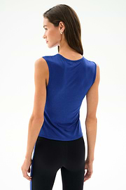 A woman with long brown hair models the SPLITS59 Nikki Jersey Tank - Cobalt, standing and facing away against a plain light background.