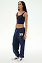 A woman is standing in SPLITS59's Serena French Terry Oversized Sweatpant in Indigo/59, crafted from soft cotton fabric, paired with a navy crop top and white sneakers against a plain white background.