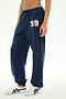 A person is wearing the SPLITS59 Serena French Terry Oversized Sweatpant in Indigo/59—crafted from 100% cotton, featuring the number 59 on the left thigh—paired with white sneakers with black stripes, standing against a plain background.