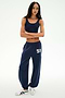 Wearing SPLITS59's Serena French Terry Oversized Sweatpant in indigo featuring the number 59 and a matching navy crop top, both crafted from soft cotton fabric, this person stands with arms crossed against a plain white background, finishing the look with classic white sneakers.