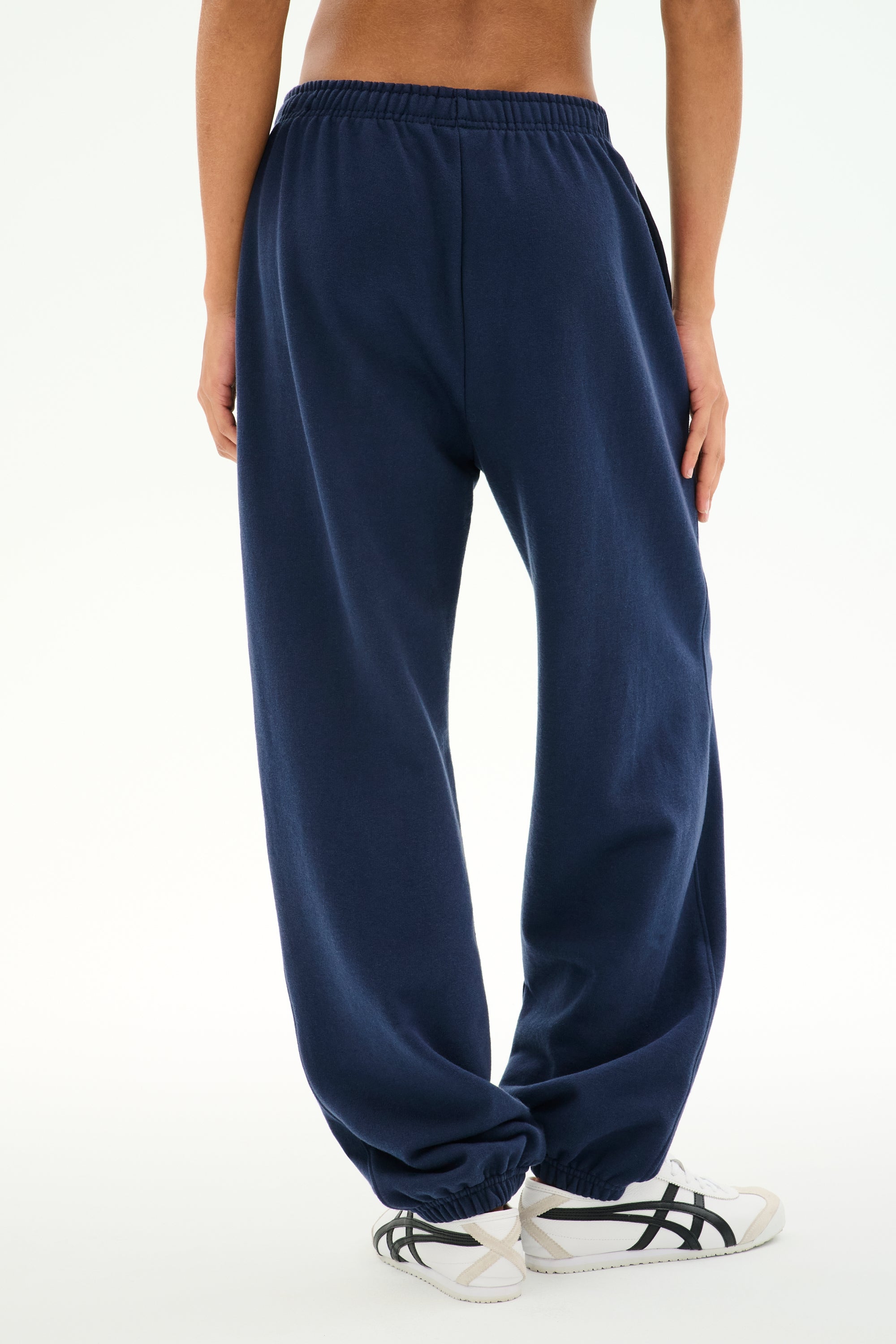 A person wearing the SPLITS59 Serena French Terry Oversized Sweatpant in Indigo/59, made from 100% cotton, and white sneakers stands on a white background with their hands relaxed by their sides.