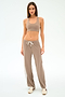 A woman faces forward in SPLITS59 Willow Airweight Wide Leg pants in Latte/White, paired with a taupe spandex sports bra and beige sneakers against a plain white background.