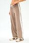 A person sports the SPLITS59 Willow Airweight Wide Leg pants in Latte/White, featuring a white side stripe, drawstring waist, and added spandex for comfort, paired with cream sneakers accented by maroon stripes.