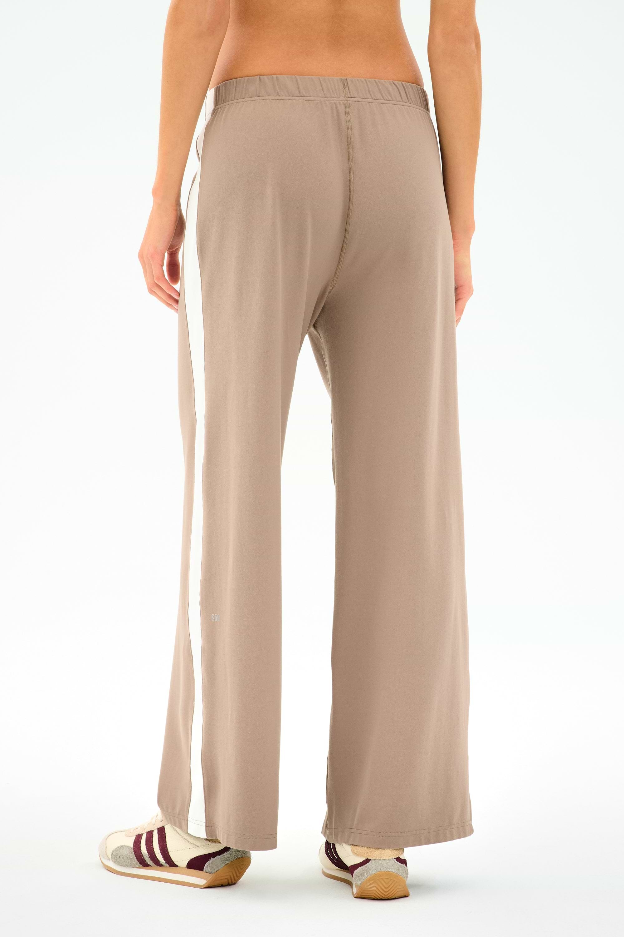 Model wears SPLITS59 Willow Airweight Wide Leg pants in Latte/White with maroon and white sneakers, shown from the back against a plain background.