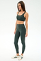 A woman wears SPLITS59's Airweight Rib High Waist 7/8 leggings in Military with a matching sports bra and white sneakers, standing against a plain white background.