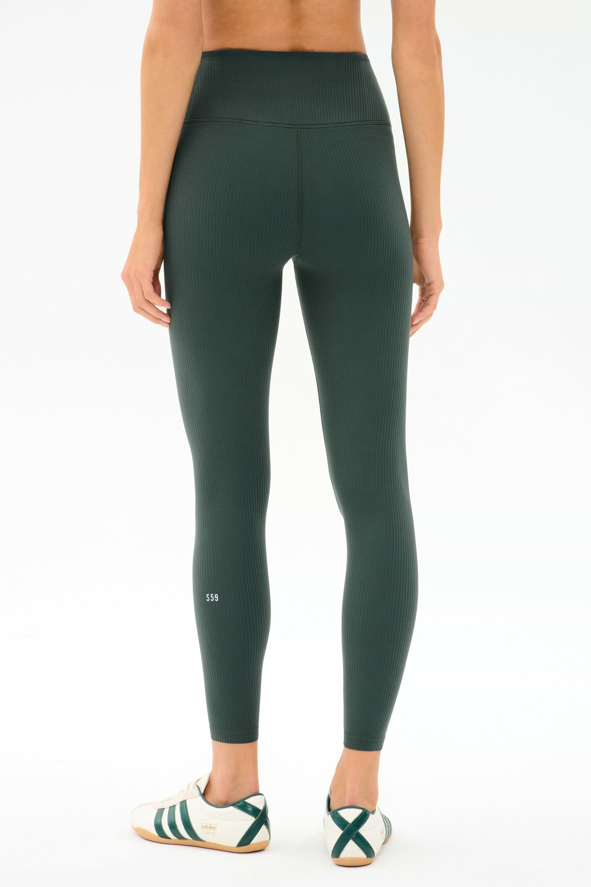 Person faces away, wearing SPLITS59 Airweight Rib High Waist 7/8 leggings in Military and white sneakers with green detail, against a plain light background.