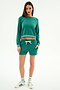 A woman stands against a white background wearing the SPLITS59 Brooks Fleece Sweatshirt With Stripe in Arugula/White, paired with matching shorts, striped socks, and white sneakers with green stripes.
