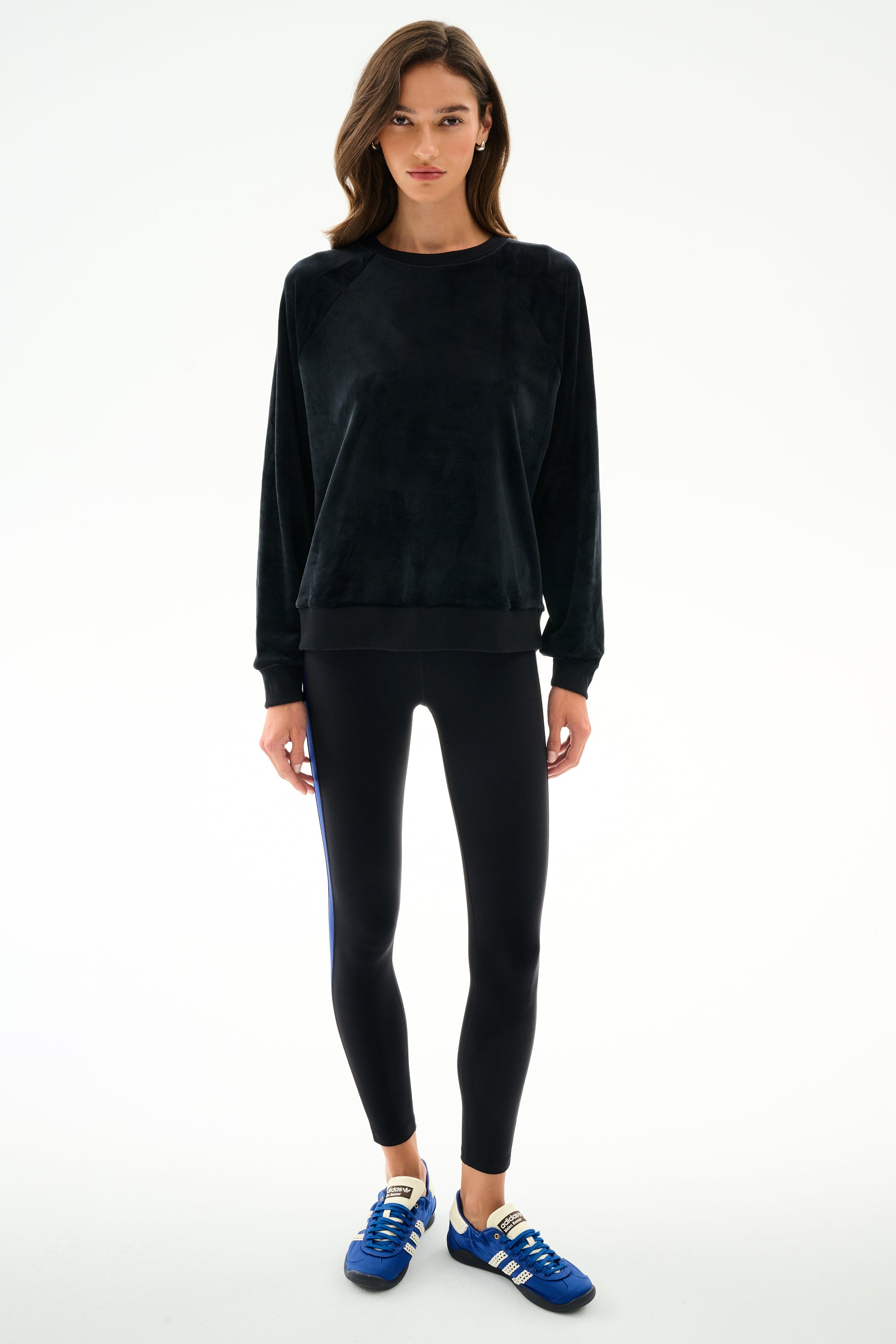 Woman stands against a white background, wearing the SPLITS59 Joy Velour Crewneck - Black with black leggings and blue sneakers.