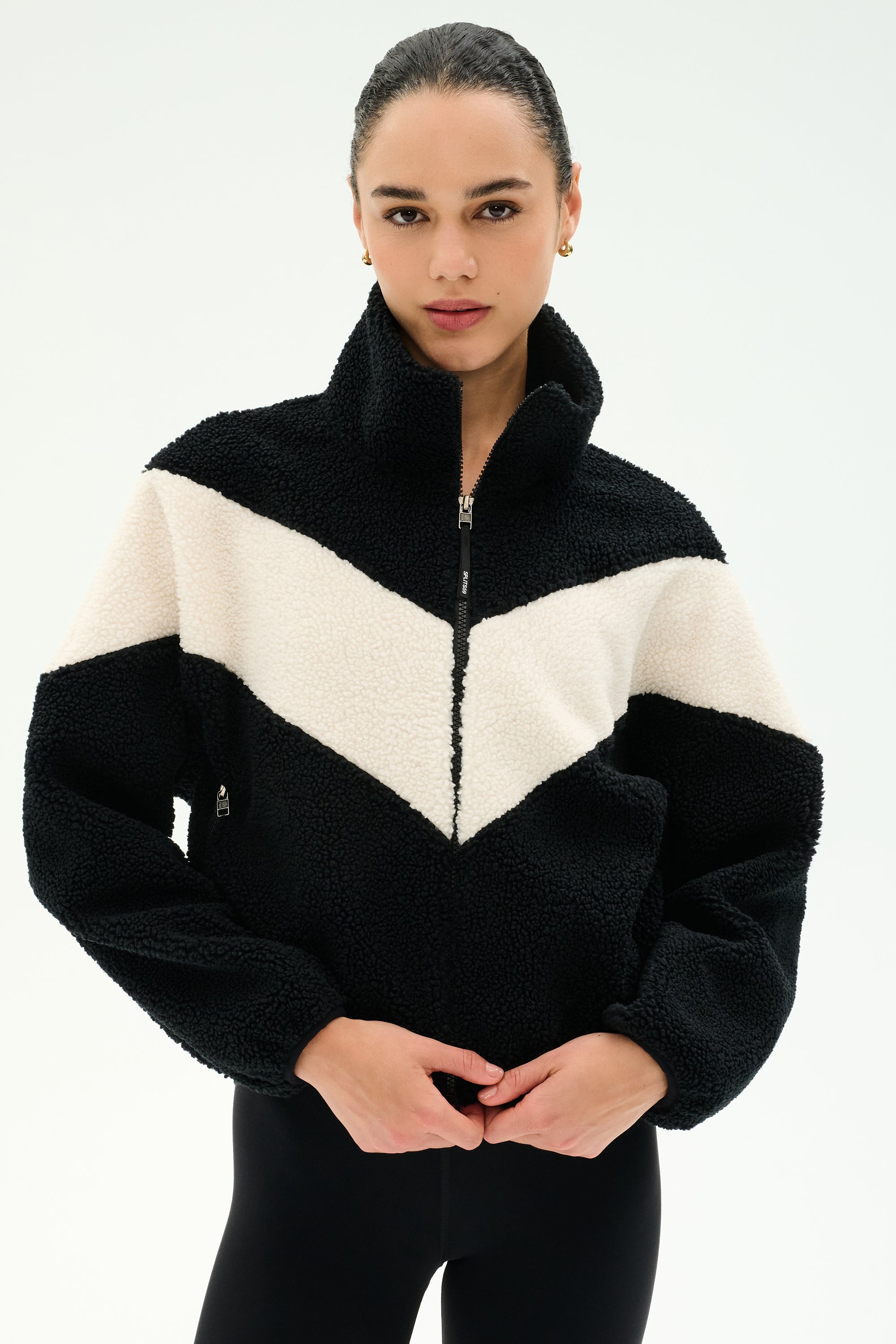 A person wearing the SPLITS59 Lottie Chevron Sherpa Full Zip Jacket in Black/Creme, made from 100% polyester, stands against a plain light background.