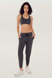 Full front view of woman with dark wavy hair wearing dark grey bra and dark drey joggers with black drawstring paired with white shoes