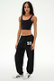 Wearing a black crop top and SPLITS59 Serena French Terry Oversized Sweatpant in Black/59—featuring the “59” detail on the left leg and made in Los Angeles—the person stands against a plain white background, paired with white sneakers.