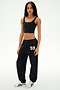 Wearing a black crop top and SPLITS59 Serena French Terry Oversized Sweatpant in Black/59—featuring the “59” detail on the left leg and made in Los Angeles—the person stands against a plain white background, paired with white sneakers.