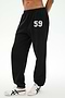 Model wears the SPLITS59 Serena French Terry Oversized Sweatpant in Black/59, featuring the number 59 printed on the left thigh. Made in Los Angeles for a comfortable and stylish look, these sweatpants are paired with white sneakers with black stripes and set against a plain background.