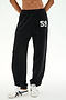 A person is wearing the SPLITS59 Serena French Terry Oversized Sweatpant in black with a “59” on the left thigh, paired with white sneakers featuring black accents, standing against a plain background; these sweatpants are made in Los Angeles.