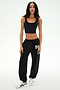 A woman stands on a white background wearing a black cropped tank, white sneakers, and the SPLITS59 Serena French Terry Oversized Sweatpant in Black/59, featuring “59” on the leg and made in Los Angeles.
