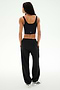 A person stands facing away with hands in pockets against a plain light background, wearing a black crop top, white sneakers, and the SPLITS59 Serena French Terry Oversized Sweatpant in Black/59, made in Los Angeles.