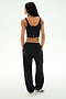 A person stands facing away with hands in pockets against a plain light background, wearing a black crop top, white sneakers, and the SPLITS59 Serena French Terry Oversized Sweatpant in Black/59, made in Los Angeles.