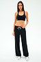 A woman wearing the SPLITS59 Willow Airweight Wide Leg pants in Black/White with a black sports bra and white sneakers stands against a white background.