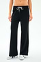 A person wearing SPLITS59's Willow Airweight Wide Leg pants in black with white side stripes and white sneakers, standing against a plain white background.