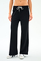 A person wearing SPLITS59's Willow Airweight Wide Leg pants in black with white side stripes and white sneakers, standing against a plain white background.