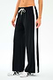 A person models the SPLITS59 Willow Airweight Wide Leg pants in Black/White, featuring buttery-soft fabric, wide legs, white side stripes, and a white drawstring, paired with white sneakers against a plain background.