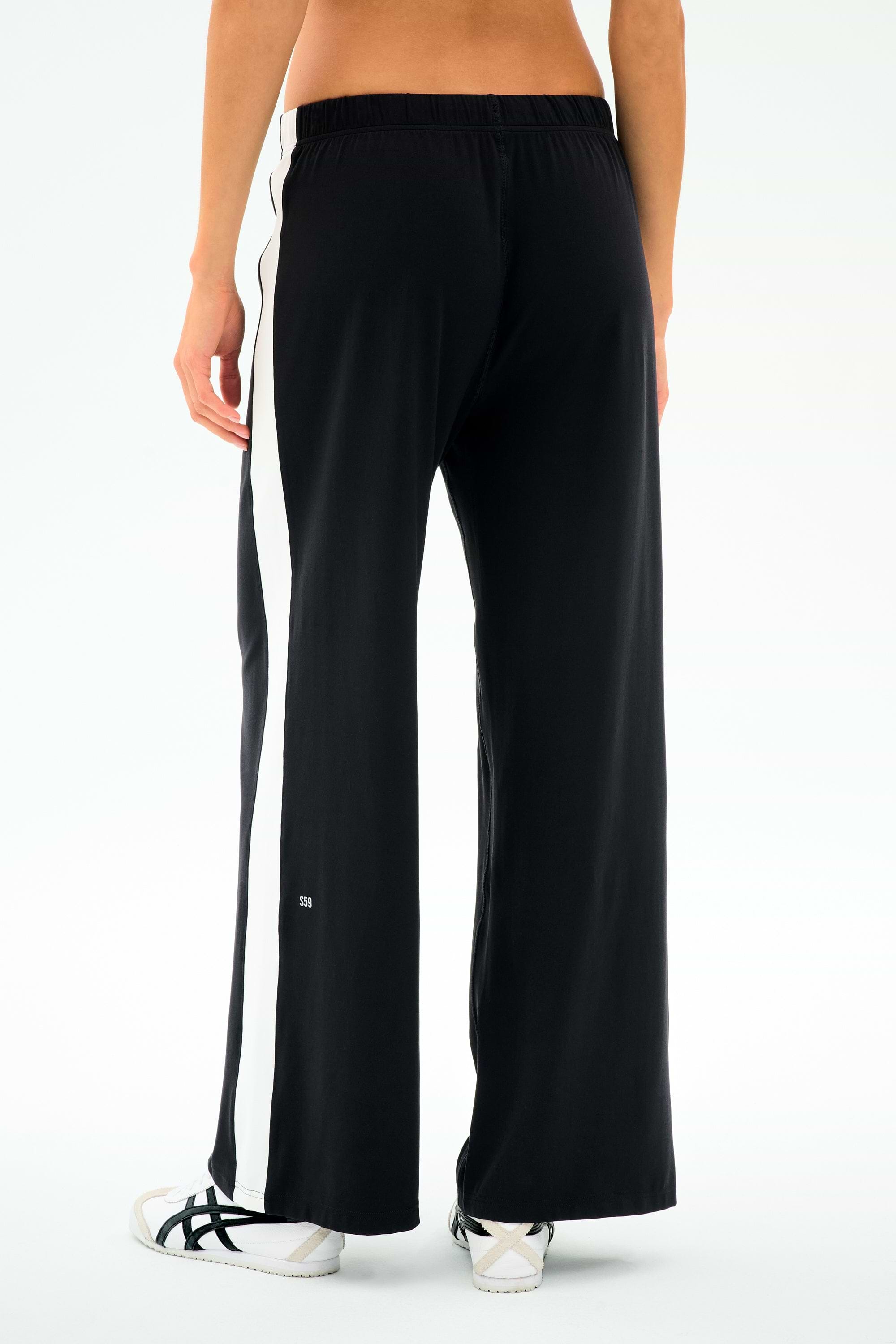 Model wears the SPLITS59 Willow Airweight Wide Leg pants in Black/White with white sneakers, shown from the back on a plain background—ideal for Pilates or casual outings.