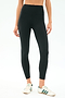 A person wears SPLITS59 Airweight Rib High Waist 7/8 leggings in black—ideal for Pilates or hot yoga—with white sneakers featuring green stripes, standing against a simple light background.