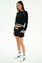 A woman wears the SPLITS59 Brooks Fleece Sweatshirt With Stripe in Black/White, paired with matching black shorts, white socks, and sneakers against a plain background.